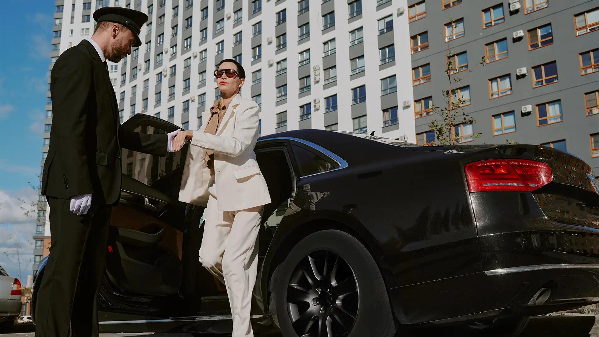 Chauffeur in a dark suit holding the rear door of a black executive sedan open on a Chicago street