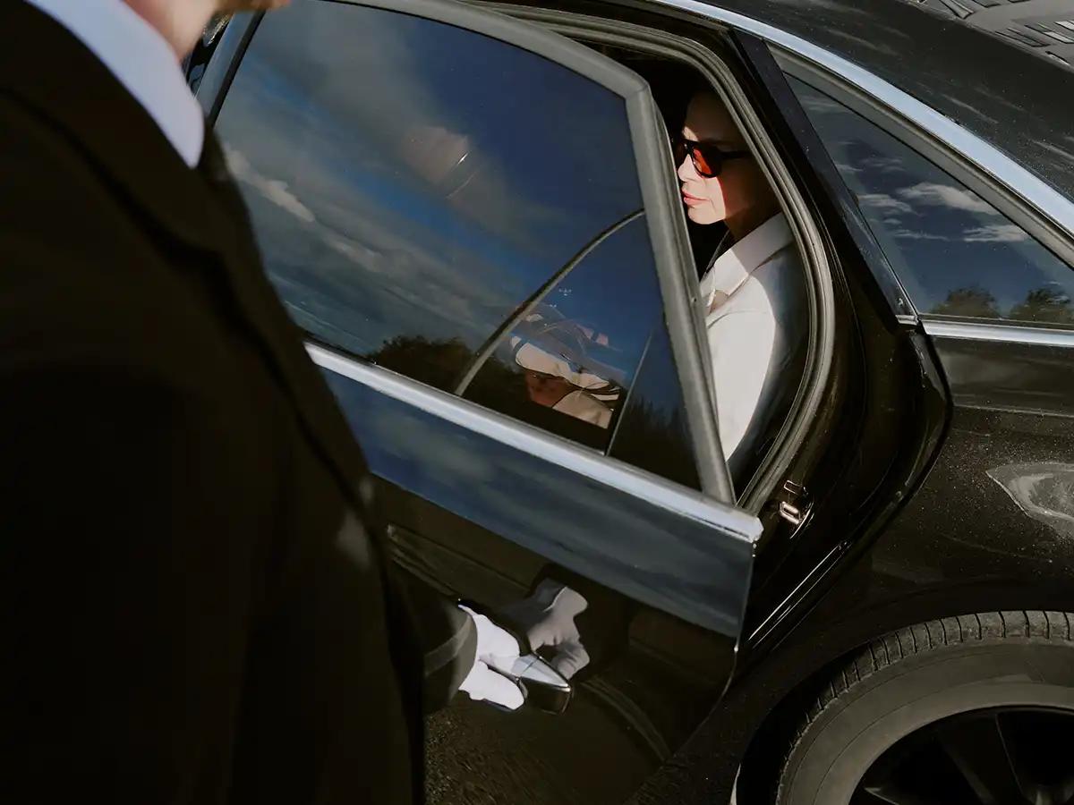 Chauffeur in a dark suit opening the rear door of a black executive sedan for a business traveller outside a Chicago hotel